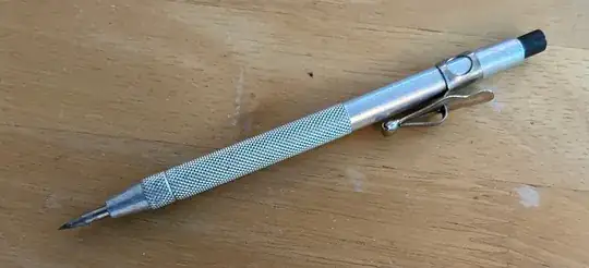 Photo of a scriber on a wooden table.  It's a pencil-shaped metal holder with a sharp tip.  Photo taken by me.