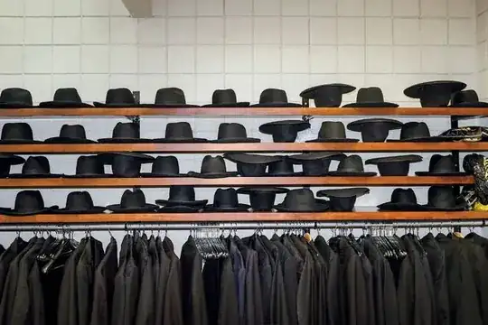 shelves of black hats and a rack of black jackets in front of a tiled wall