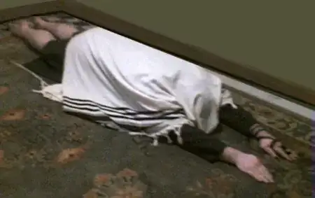 picture of a man in talis and tefillin, laying flat on the ground, with his arms stretched out in front of him