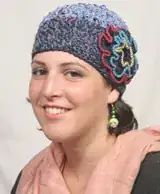 another woman with a hat on her head, with hair coming out the bottom of the hat both down the back of her head and her neck and a little at her temple
