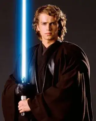 Publicity still of Anakin from "Revenge of the Sith." Anakin stands in Jedi robes facing the viewer, holding his lightsaber vertically in a two-handed grip in front of his right shoulder.  His left hand is on the hilt at waist level, his gloved right hand above it.