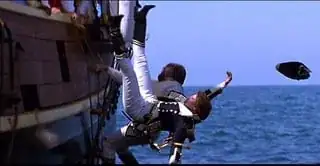 Dr. Crusher and Worf, in period attire, fall from the deck of a 18th century warship in a simulated sea environment.