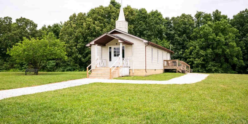 Small white chapel with a steeple, surrounded by greenery.