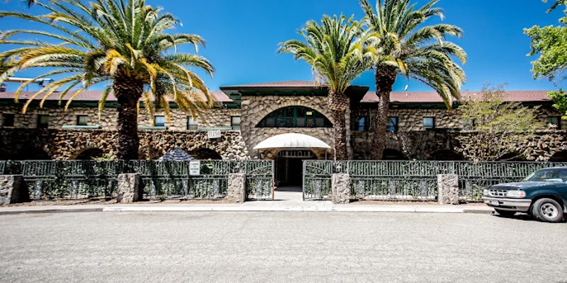 Exterior of a stone rehab facility with palm trees and gated entrance.