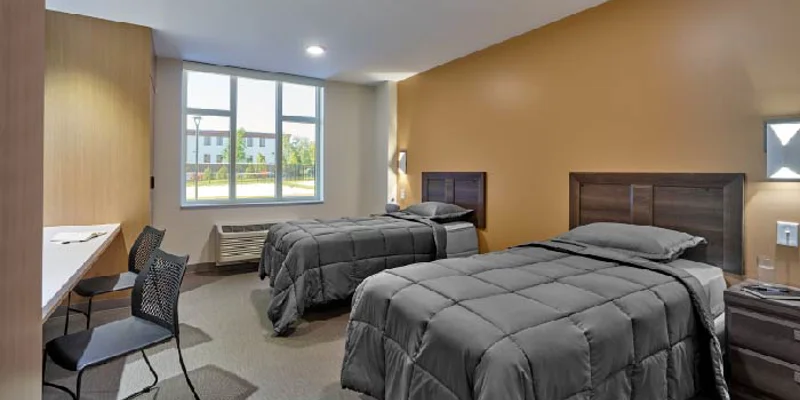 Shared bedroom with two twin beds, sidetables and a long desk.