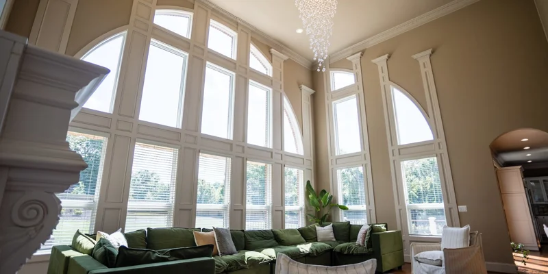 A stylish lounge with a large green sectional under tall arched windows
