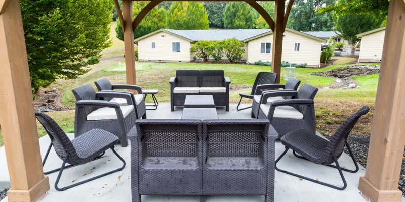 A gazebo with outdoor seating, surrounded by greenery and cottages.