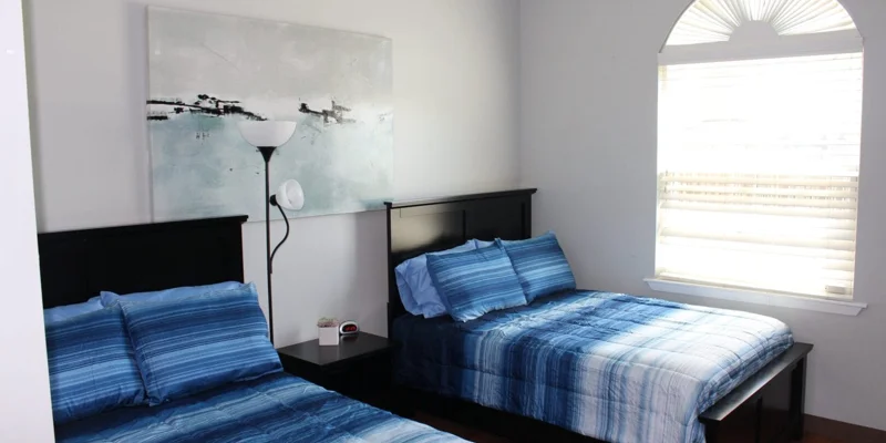Bedroom with two  beds, a large window and wall art.