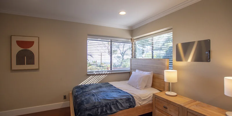 Minimalist bedroom with a wooden bed, soft lighting, and large windows