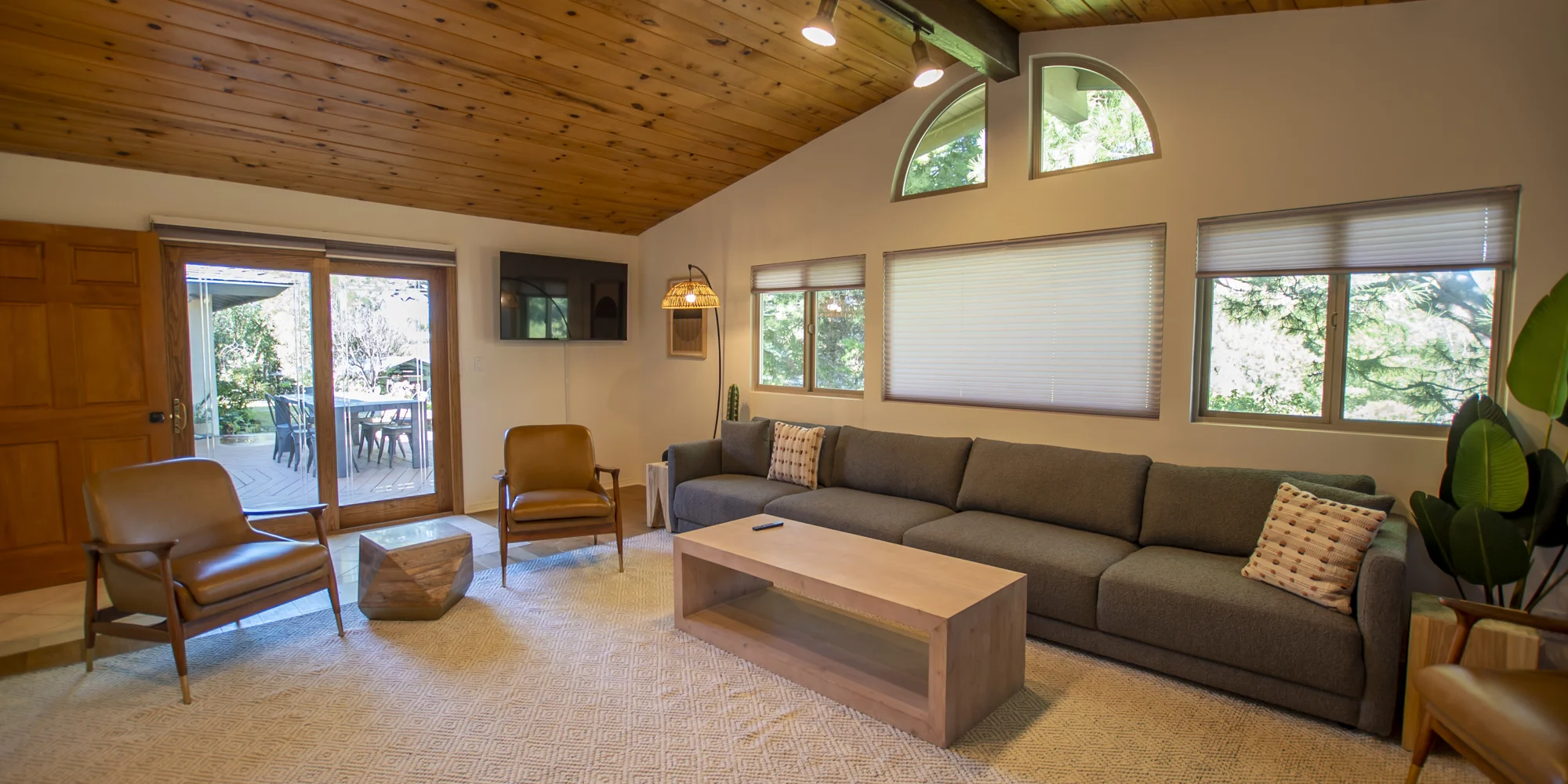 A living room with vaulted ceilings, large windows, and a gray sofa.