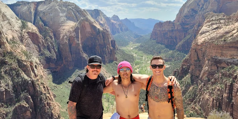 Three men pose together on a mountaintop with a canyon view behind.