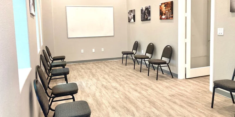 A bright group therapy room with chairs facing a whiteboard.