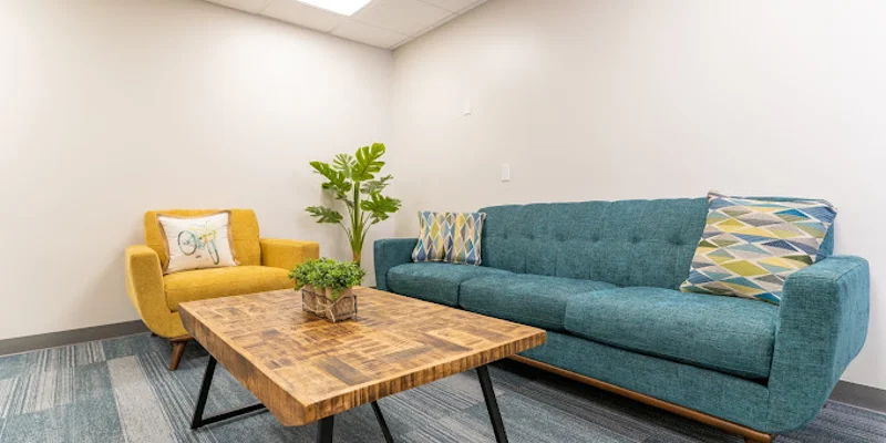 Waiting area with a blue couch, yellow chair, and wooden coffee table.