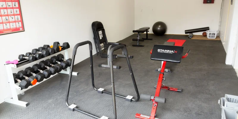 A small gym with weights, exercise equipment, and mats.
