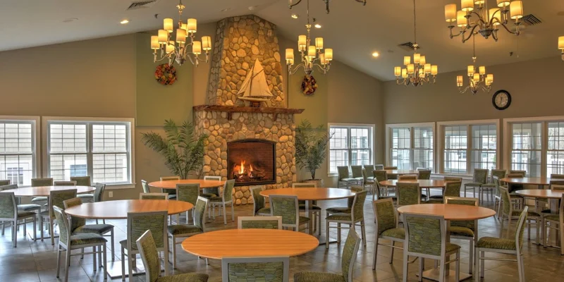 A dining hall with a lit fireplace, round tables, and chandeliers.