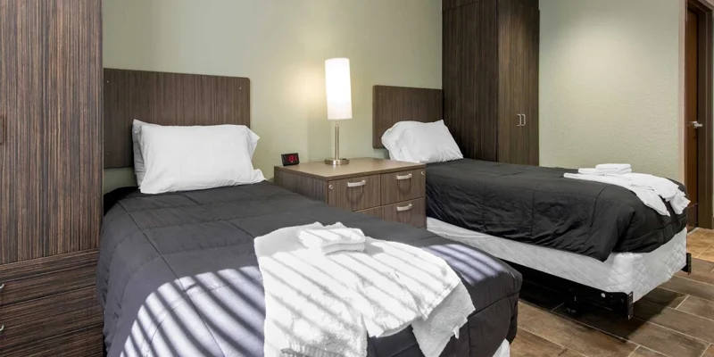 A rehab bedroom with two beds, dark wood furniture, and a bedside lamp.