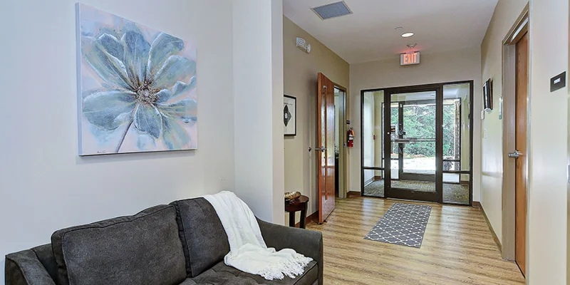 Lobby hallway with gray couch, artwork, and glass entrance door.