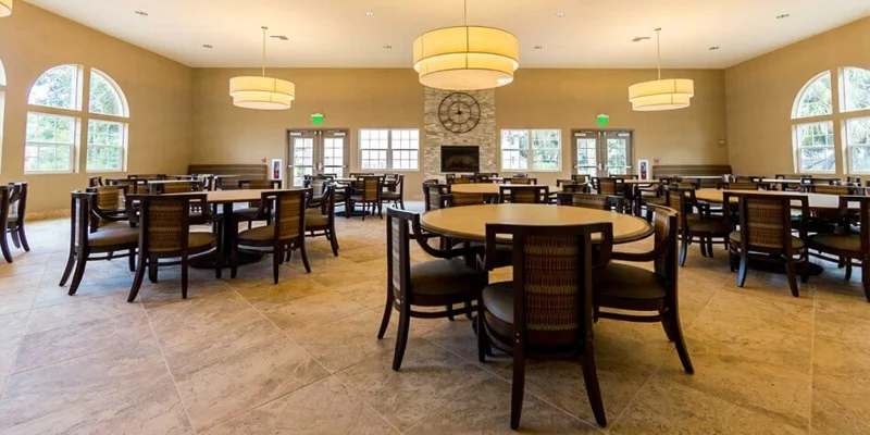 A spacious dining hall with large windows and round tables.