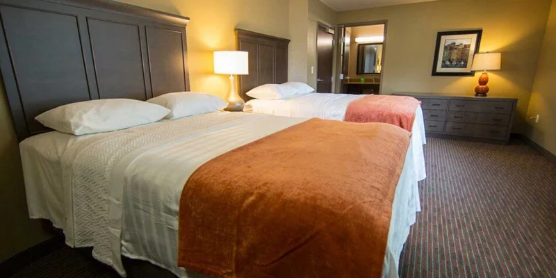 A bedroom with two large beds, orange blankets, and warm lighting