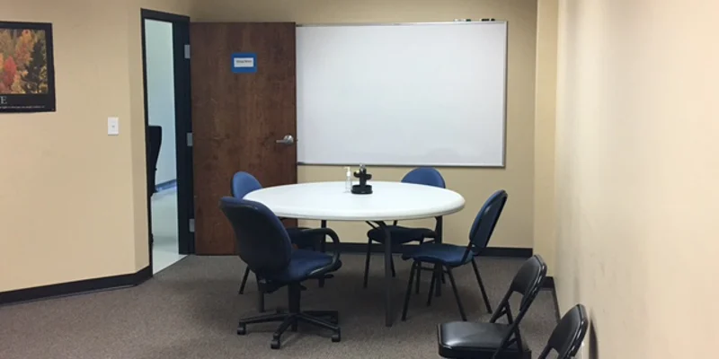 A group meeting room with a round table, chairs, and a whiteboard.