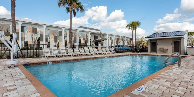 Outdoor pool area with lounge chairs and palm trees under a blue sky.