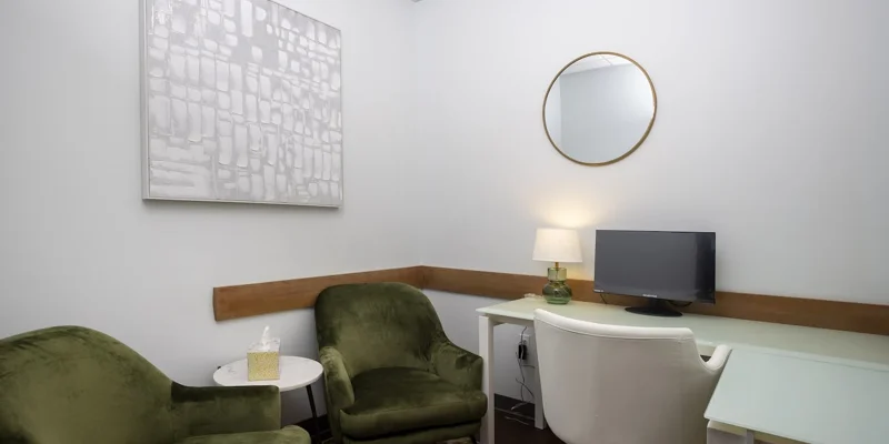 A small office with green chairs, white desk, and a computer setup