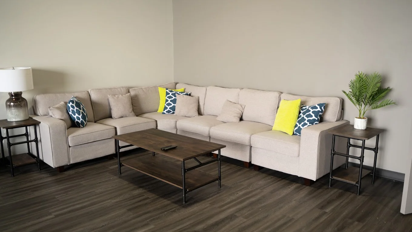  lounge area with a beige couch, wooden tables, and a modern design.