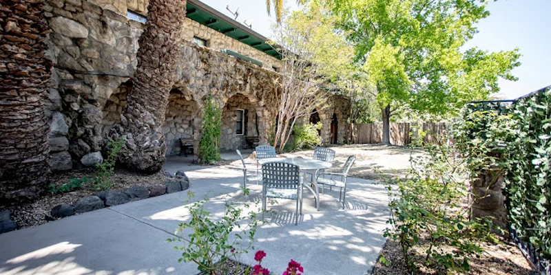 An outdoor patio with tables, chairs, stone walls, and lush greenery.