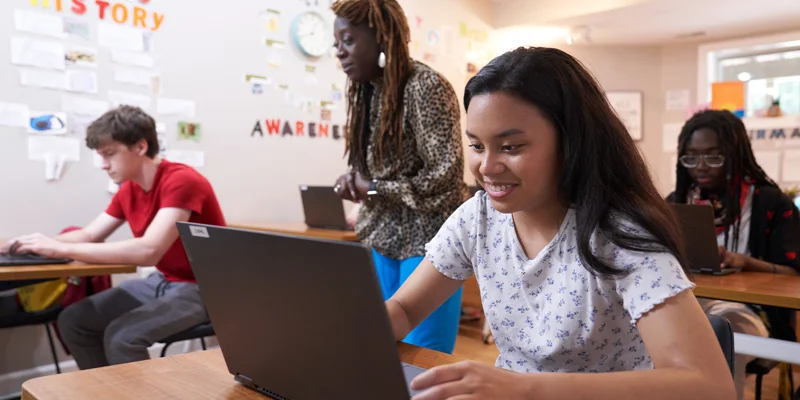Teens working on laptops in a classroom with a teacher