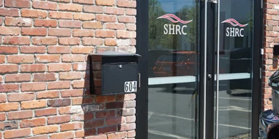 Outdoor view of building’s entrance with parking lot. ​​