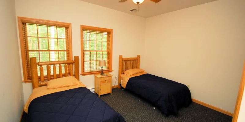 A shared bedroom with two wooden twin beds and natural light