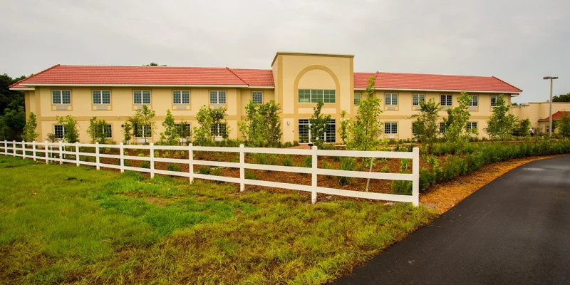 A large two-story rehab facility with a red roof and a white fence
