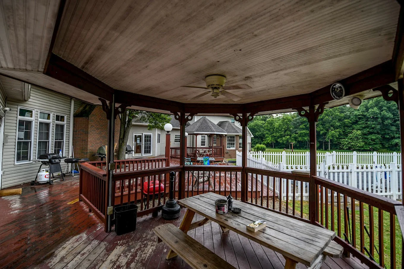 Covered gazebo with a picnic table overlooking a deck and white fence.