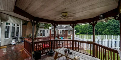 Covered gazebo with a picnic table overlooking a deck and white fence.