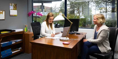 A therapist and a client in a counseling session at a wooden desk.