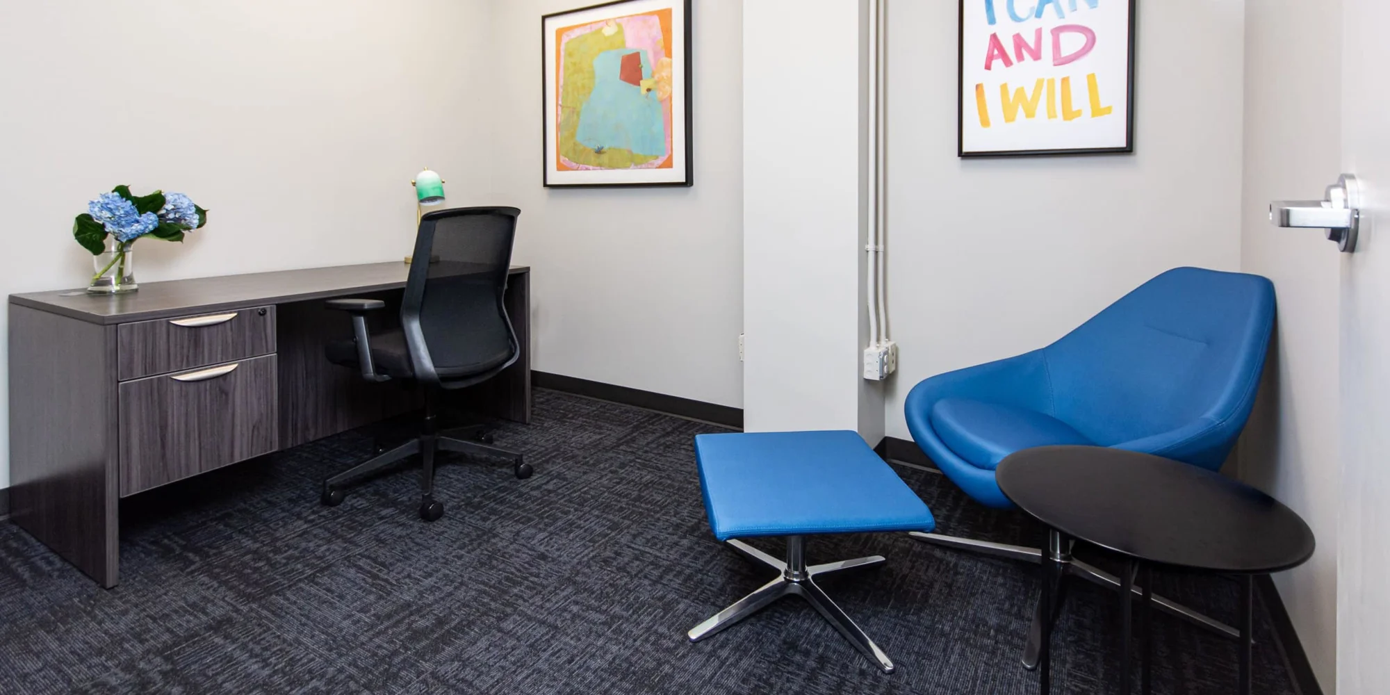 A small office with blue chairs and modern wall art.