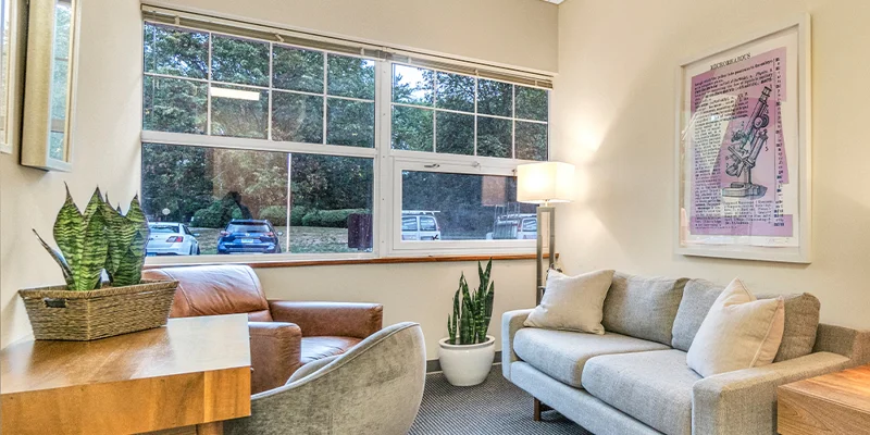 Therapy room with a sofa, chair and a desk.