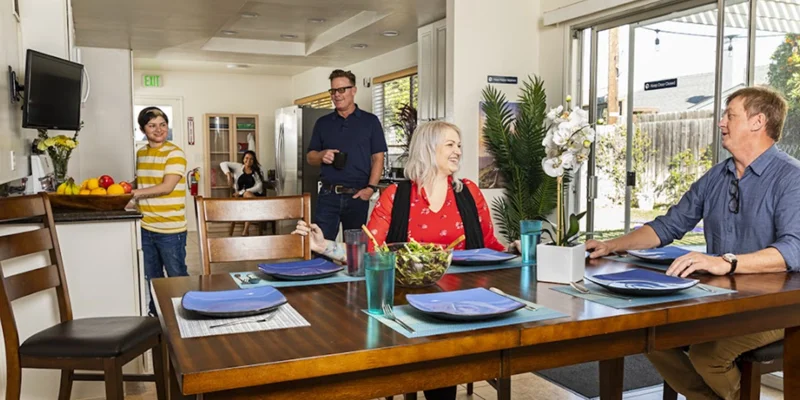 Rehab facility dining area with a wooden table, chairs, and bright lighting.