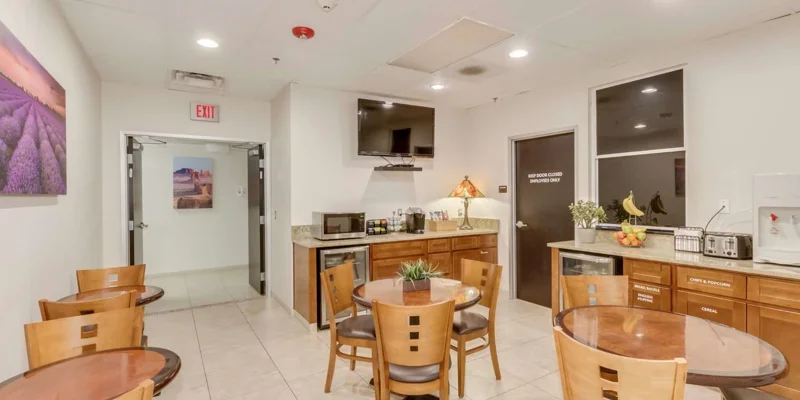 Dining area with tables and chairs arraged next to kitchen with a TV.
