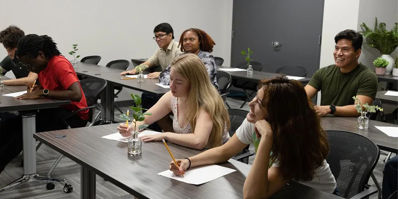 A group of people taking notes in a room with grey flooring.