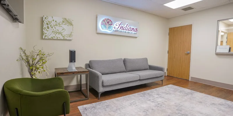 Waiting area with a gray couch, green chair, and Indiana sign on the wall.