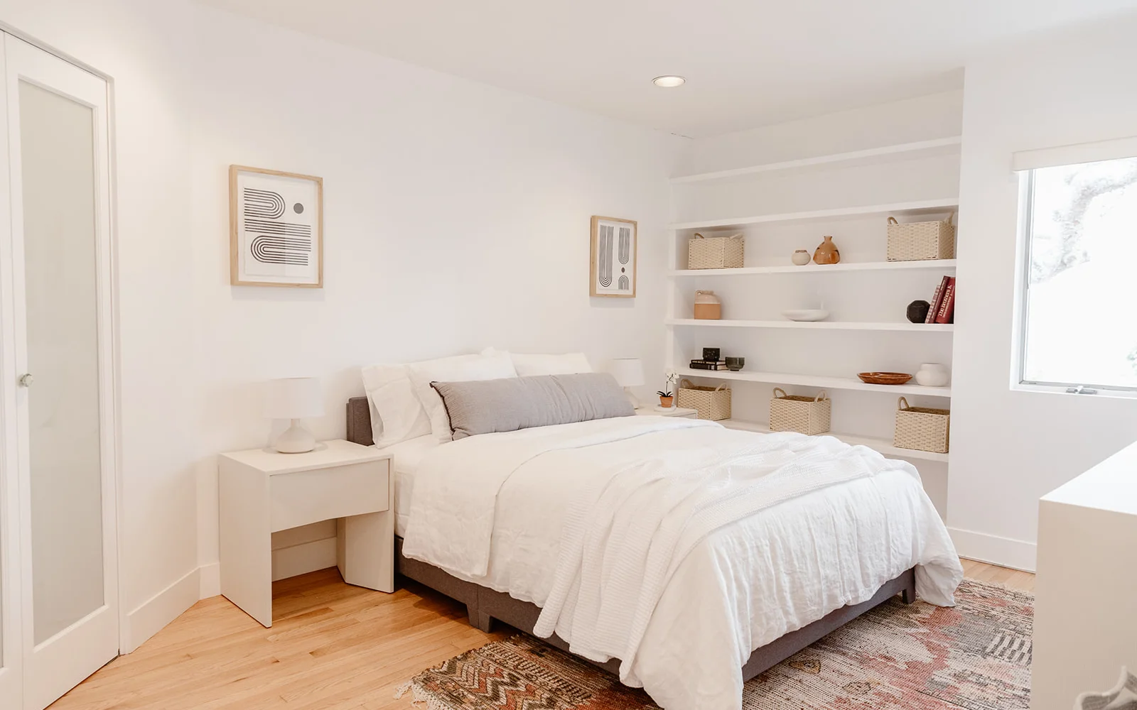  Minimalist bedroom with white decor, built-in shelving, and natural light.