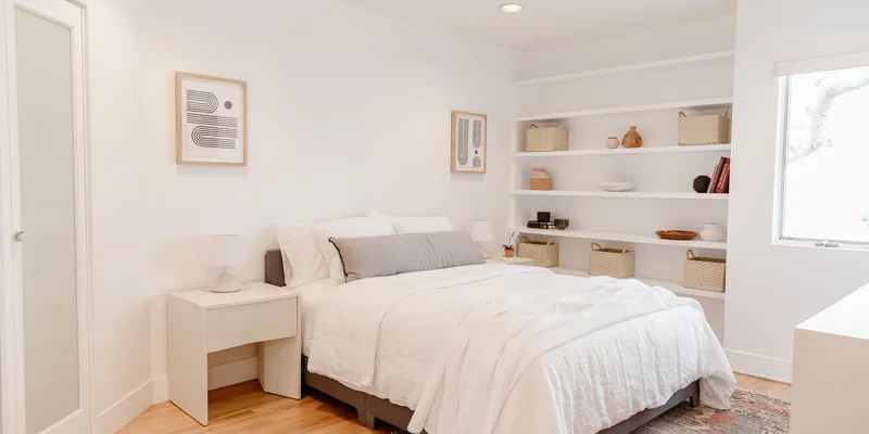  Minimalist bedroom with white decor, built-in shelving, and natural light.