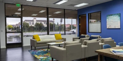 Rehab center lounge with large windows, neutral seating, and a blue wall.
