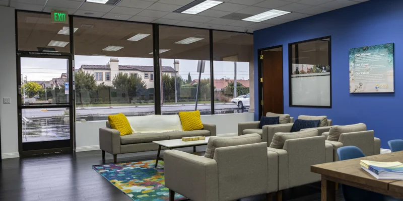 Rehab center lounge with large windows, neutral seating, and a blue wall.