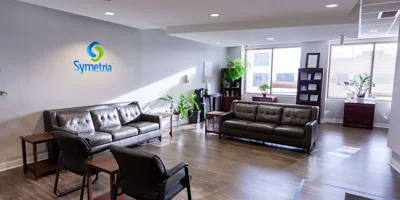 A waiting area with black leather sofas, chairs, and potted plants.