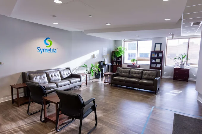 A waiting area with black leather sofas, chairs, and potted plants.