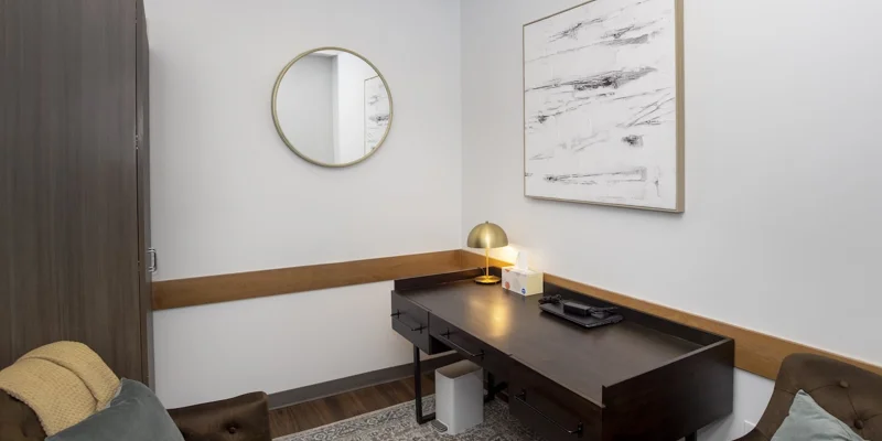 A sleek office with a dark wooden desk, chair, and round mirror