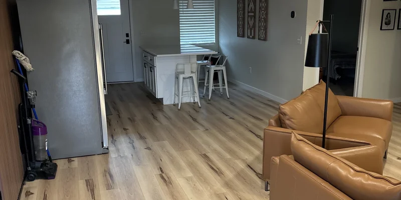 Open kitchen-living space with island, fridge, and tan armchairs.