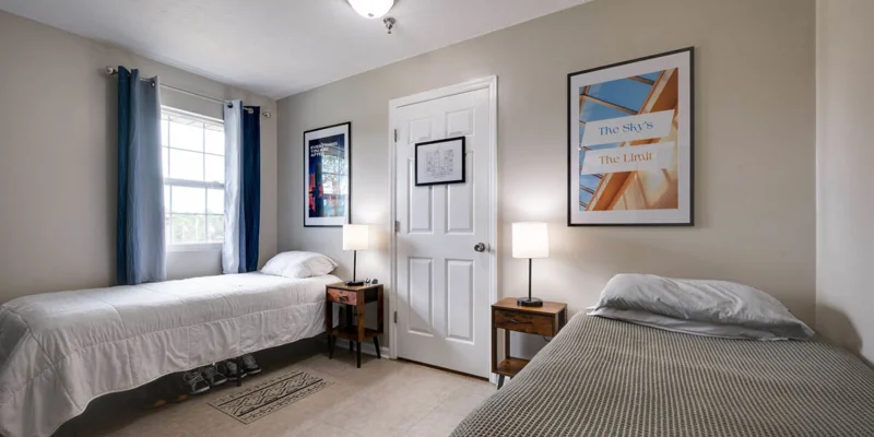 Twin bedroom with a window, blue curtains, and framed wall art.
